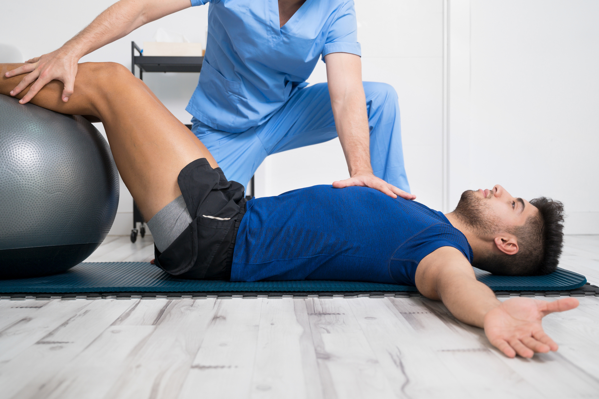 Physiotherapeut begleitet einen Patienten bei einer Übung mit Gymnastikball